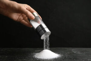 Woman pouring salt from shaker onto black table, closeup