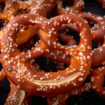 A pretzel with extra pretzel salt on top of a stack of pretzels