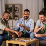 3 men relaxing together, they are drinking beer and playing a card game