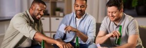 3 men relaxing together, they are drinking beer and playing a card game