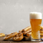 a glass of beer next to a stack of pretzels
