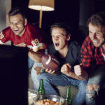 Three men excitedly watching their football team play on TV