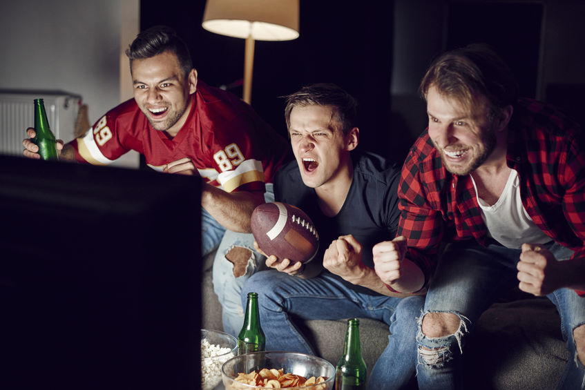 Three men excitedly watching their football team play on TV