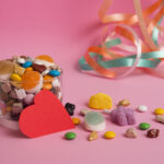 A clear glass filled with different candies, with a red paper heart leaning on it