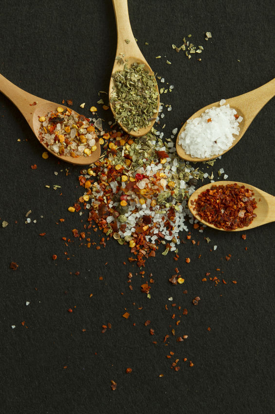 Four spoons with different spices and salt on a black background