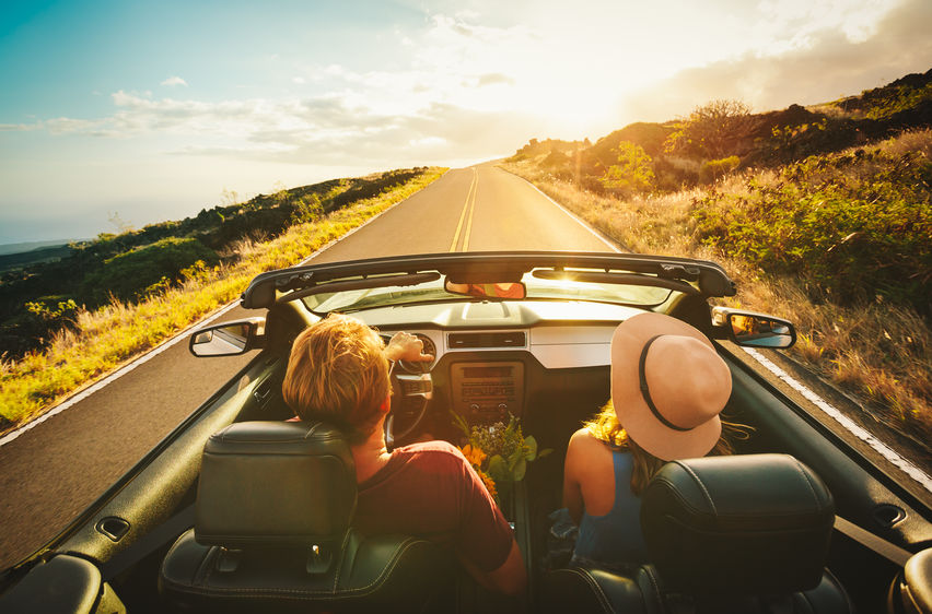 Happy Young Couple Driving Along Country Road in Convertible at Sunset