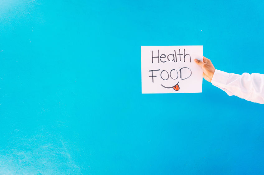 A female hand holding a paper with the writing "health food" on the blue background