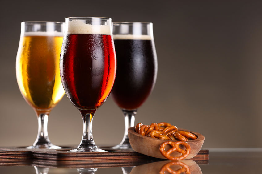 Glasses with different types of beer and pretzels on mirror surface, closeup. Space for text