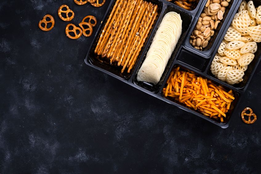 A variety of snacks in a box, including pretzels on a concrete black table